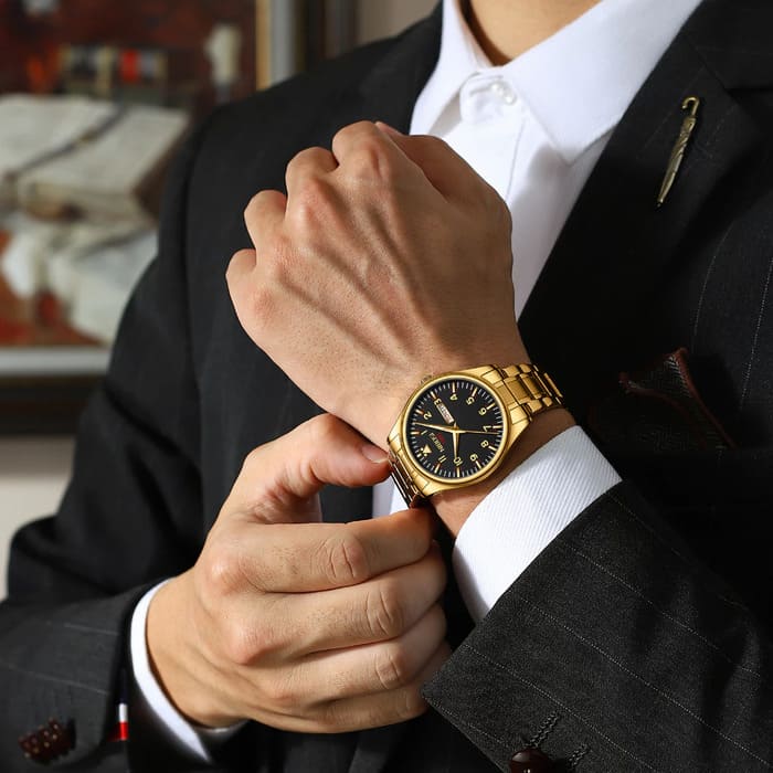Relógio Nibosi masculino Syncro com pulseira de aço inoxidável dourada e visor preto no pulso de um homem