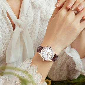 Relógio feminino Nibosi Nataly com pulseira de couro marrom e mostrador branco no pulso de uma mulher