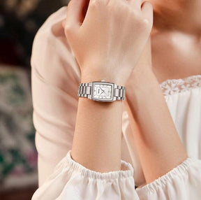 Relógio feminino minimalista pequeno com pulseira prata e visor branco no pulso de uma mulher