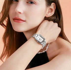 Relógio feminino minimalista pequeno com pulseira prata e visor branco no pulso de uma mulher
